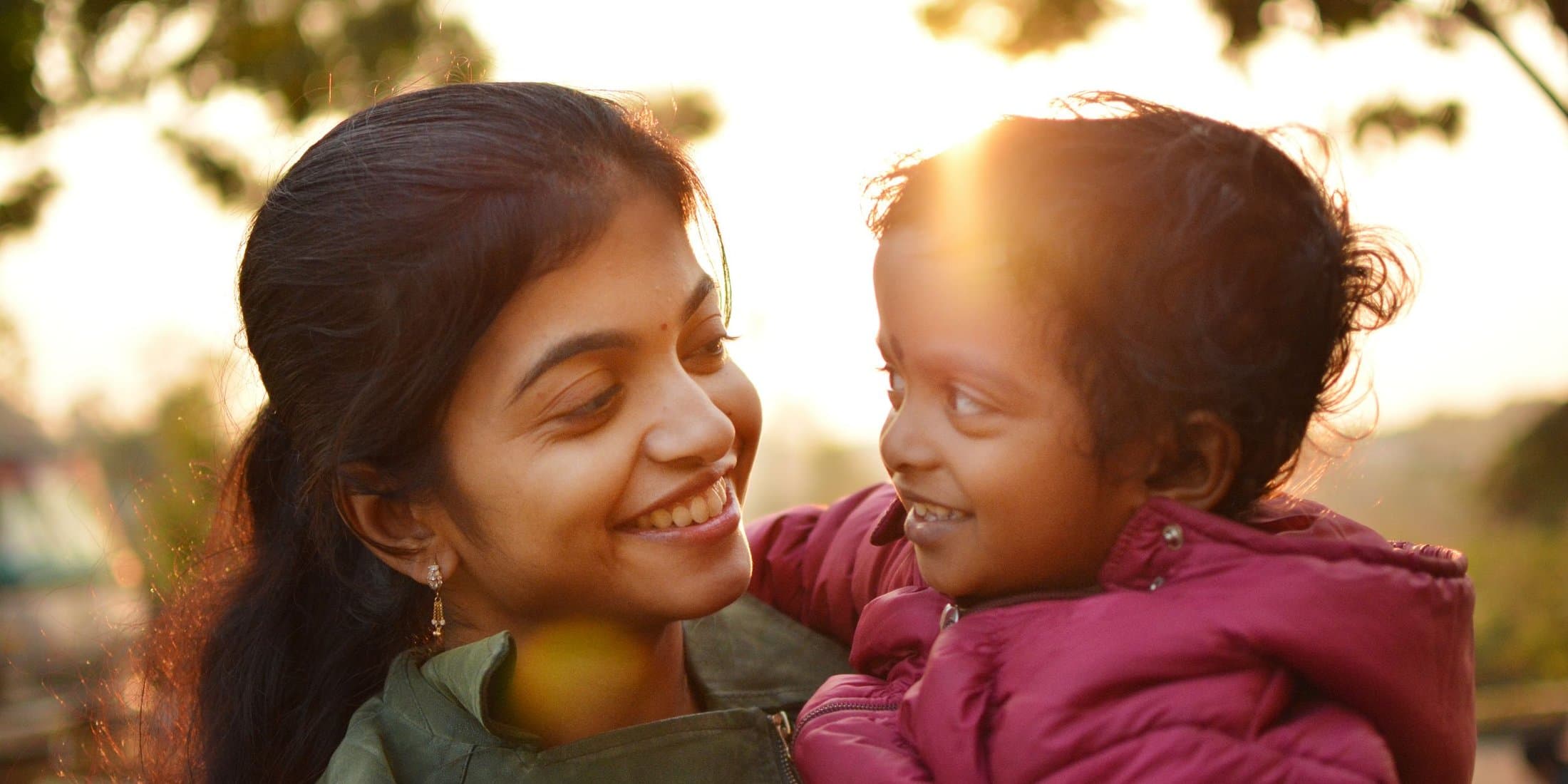 A mother and daughter smiling warmly at each other at golden hour